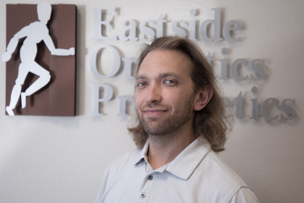 Ben J is grinning at the camera in a confident manner in front of the Eastside O & P sign.